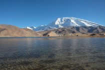 Increíble paisaje con el lago Karakul y montañas cubiertas de nieve en el día soleado - foto de stock