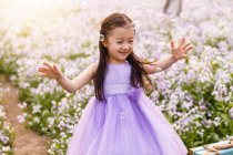 Очаровательный азиатский ребенок в платье ловит мыльные пузыри на цветочном поле — стоковое фото