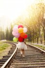Вид сзади ребенка, идущего по железной дороге с кучей воздушных шаров — стоковое фото