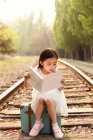 Adorabile asiatico bambino seduta su viaggio borsa e lettura libro — Foto stock