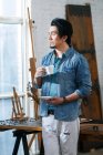 Зайнятий азіатський чоловік тримає чашку кави і дивиться в художню студію — стокове фото