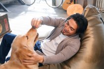 Alto ângulo vista de feliz asiático homem jogar com cão no casa — Fotografia de Stock