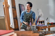 Thoughtful young male painter looking at picture in studio — Stock Photo