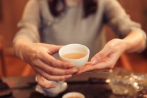 Cropped shot of woman holding white cup with hot aromatic herbal tea — Stock Photo