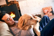 Handsome asian man lying on bean bag chair and hugging dog at home — Stock Photo