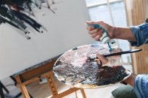 Plano recortado de artista masculino sosteniendo paleta con tubo de pintura en el estudio - foto de stock