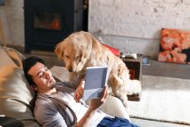 Високий кут зору молодого азіатського чоловіка читає книгу і грає з собакою вдома — стокове фото