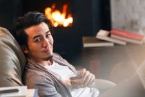 Selektiver Fokus eines gut aussehenden asiatischen Mannes, der ein Glas Whiskey in der Hand hält und zu Hause in die Kamera lächelt — Stockfoto