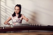 Smiling young asian woman playing traditional chinese guzheng string instrument — Stock Photo