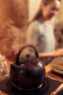 Close-up view of boiling teapot with steam and young asian woman on background, selective focus — Stock Photo