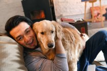 Feliz asiático homem abraçando cão e sorrindo para câmera em casa — Fotografia de Stock