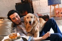 Alegre asiático hombre descansando con perro y sonriendo a cámara en casa - foto de stock