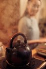 Крупним планом вигляд киплячого чайника з парою і молодою азіаткою позаду, вибірковий фокус — стокове фото