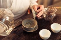 Обрізаний знімок жінки, що тримає чайник і заливає воду в порцелянову тару — стокове фото