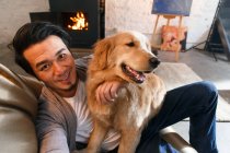 Blick aus der Vogelperspektive auf einen fröhlichen asiatischen Mann, der mit Hund ausruht und zu Hause in die Kamera lächelt — Stockfoto