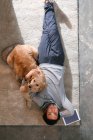 Вид сверху на человека, лежащего с собакой на ковре и смотрящего в камеру — стоковое фото