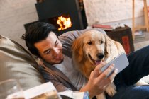 Щасливий азіатський чоловік обіймає собаку і використовує смартфон вдома — стокове фото
