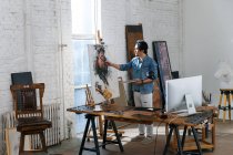 Artista maschio focalizzato in grembiule tenendo tavolozza e ritratto di pittura in studio — Foto stock
