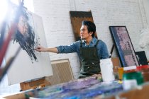 Fokussierte junge männliche Künstler in Schürze Malerei Porträt im Atelier — Stockfoto