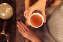 Cropped shot of woman holding cup with hot herbal tea — Stock Photo