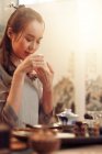 Schöne lächelnde junge asiatische Frau mit geschlossenen Augen hält Tasse und duftenden aromatischen Tee — Stockfoto