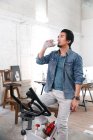 Молодий азіатський чоловік сидить на фізичному велосипеді і п'є воду вдома — стокове фото