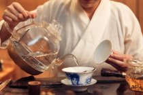 Abgeschnittene Aufnahme einer Frau, die eine Teekanne hält und Wasser in ein Porzellangefäß gießt — Stockfoto