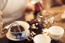 Colpo ritagliato di donna versando acqua nella tazza di porcellana con il tè — Foto stock