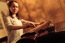 Vista basso angolo di giovane donna asiatica suonare tradizionale cinese guzheng strumento — Foto stock