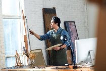 Fokussierter männlicher Künstler hält Palette und Gemälde im Atelier — Stockfoto