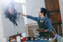 Concentrated male artist in apron painting portrait on studio — Stock Photo