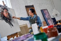 Serious young asian artist painting portrait in art studio — Stock Photo