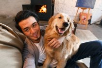 Blick aus der Vogelperspektive auf einen fröhlichen asiatischen Mann, der mit Hund ausruht und zu Hause in die Kamera lächelt — Stockfoto