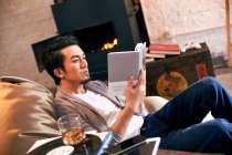 Concentré jeune asiatique homme reposant dans haricot sac chaise et lecture livre à la maison — Photo de stock
