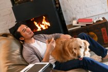 Handsome asian man holding glass of whiskey and resting with dog at home — Stock Photo