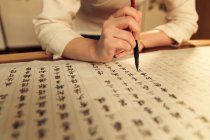 Tiro recortado de mulher segurando escova de caligrafia e escrever caracteres chineses — Fotografia de Stock