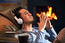 Vista lateral do homem relaxado bonito ouvindo música em fones de ouvido e olhando para cima em casa — Fotografia de Stock