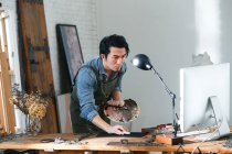 Beau peintre asiatique tenant palette et en utilisant un ordinateur de bureau en studio — Photo de stock