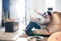 Вид збоку людини, що сидить на стільці для мішків з бобами і використовує гарнітуру віртуальної реальності вдома — стокове фото