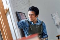 Selektiver Fokus konzentrierter asiatischer Künstler, der Porträt im Atelier malt — Stockfoto