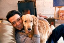 Щасливий азіатський чоловік обіймає собаку і посміхається на камеру вдома — стокове фото