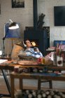 Close-up view of art tools and young man in headphones sitting near fireplace, selective focus — Stock Photo