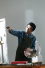 Фокусований чоловічий художник тримає палітру і картини в студії — стокове фото