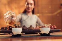Primer plano vista de joven asiático mujer verter té en taza - foto de stock