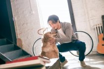 Веселий молодий азіатський чоловік погладжує смішного собаку вдома — стокове фото