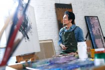 Вибірковий фокус молодого художника-чоловіка в фартуху, який дивиться на картину в студії — стокове фото