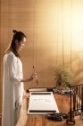 Vista lateral de jovem mulher asiática segurando escova e escrevendo caracteres chineses — Fotografia de Stock