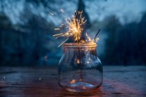 Close-up view of glass jar with burning sparklers on blurred festive background — Stock Photo