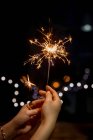 Cropped shot of person holding burning sparkler on blurred festive background — Stock Photo