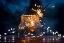 Close-up view of glass jar with burning sparklers on blurred festive background — Stock Photo